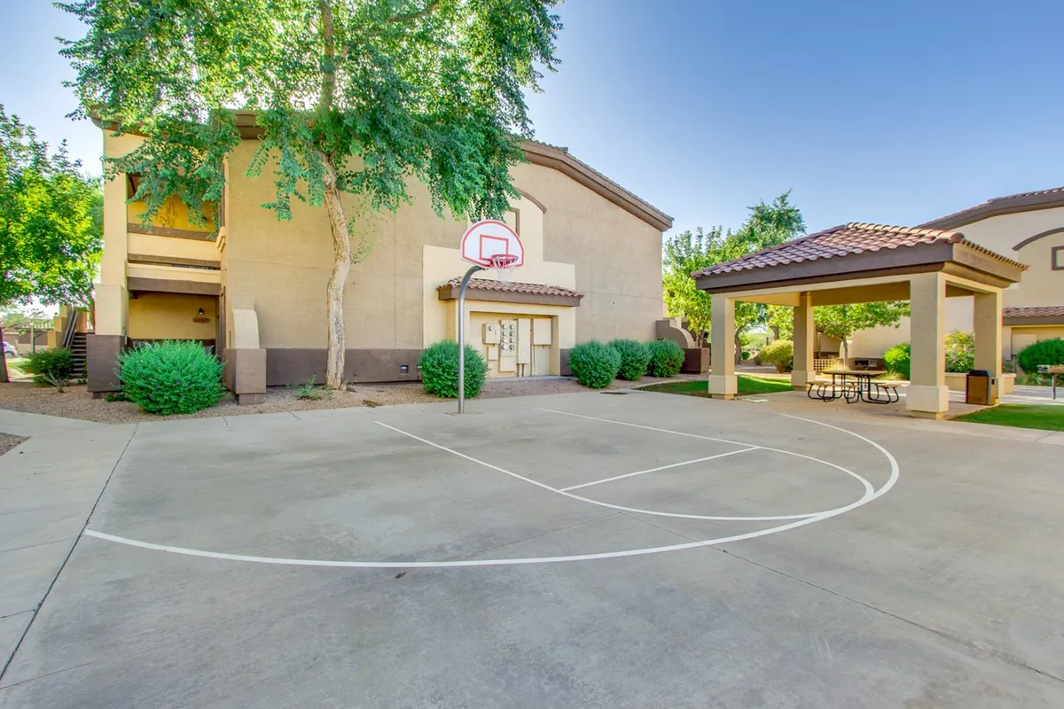A lively exterior space featuring a basketball hoop, a picnic area, and the complex's facade, inviting families to socialize, play, and enjoy community events just steps from their door.