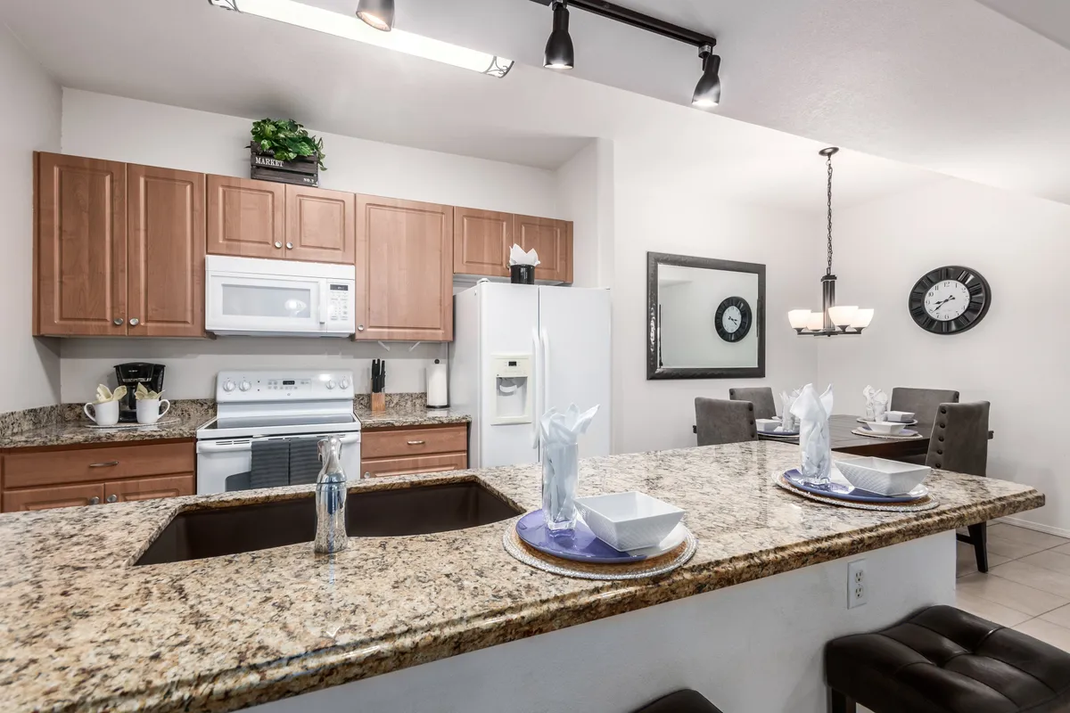 A modern kitchen with granite countertops, stylish cabinetry, and a visible dining area, warmly lit by contemporary lighting fixtures. The inviting layout suggests ample space for preparing and sharing meals, while the kitchen’s design highlights updated appliances and a cozy, homey atmosphere.