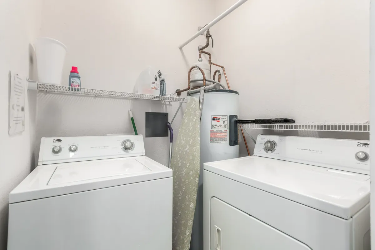 A practical laundry area featuring a washing machine, drying machine, and a shelf stocked with laundry supplies. The setup is convenient and easily accessible, making extended stays effortless.