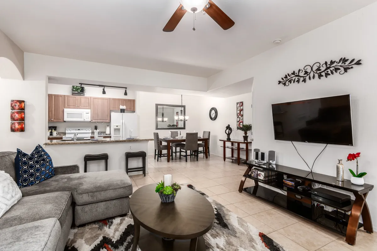 A wide view of the open-concept living and dining area featuring a plush sofa, coffee table, TV, and a dining table. There's an abundance of natural light pouring in, and the layout encourages both relaxation and togetherness. The scene feels cozy and inviting, ideal for both quiet evenings and lively gatherings.