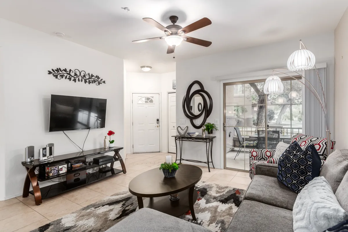 A bright, comfortable living room with a plush sofa, coffee table, smart TV on the wall, and decorative accents. A sliding glass door offers serene views of the garden, flooding the space with soft natural light and providing a tranquil connection to the outdoors.