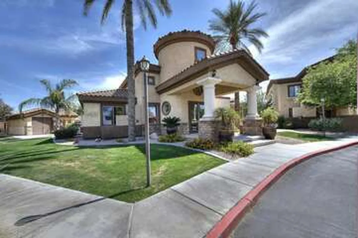 An inviting exterior entrance featuring stately columns, manicured landscaping, palm trees, and decorative architectural details, creating a serene and welcoming atmosphere. The scene hints at a secure, high-quality residential community ideal for evening strolls and a sense of retreat.