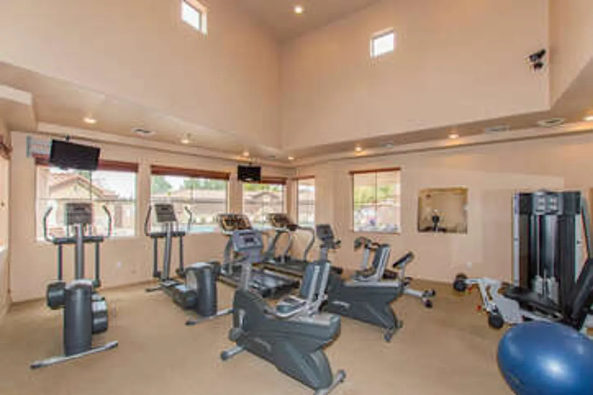 A well-equipped fitness center filled with modern exercise equipment, large windows letting in natural light, and TVs mounted on the walls. The space is bright, open, and designed for active living.