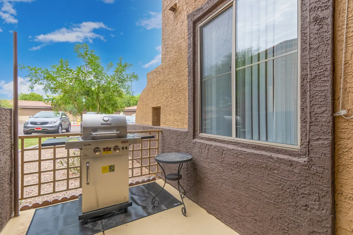 A cozy backyard patio featuring a grill and a small table, set against the backdrop of a window and outdoor greenery. The space is ideal for family barbecues, outdoor dining, or unwinding after a day of adventures around Mesa.