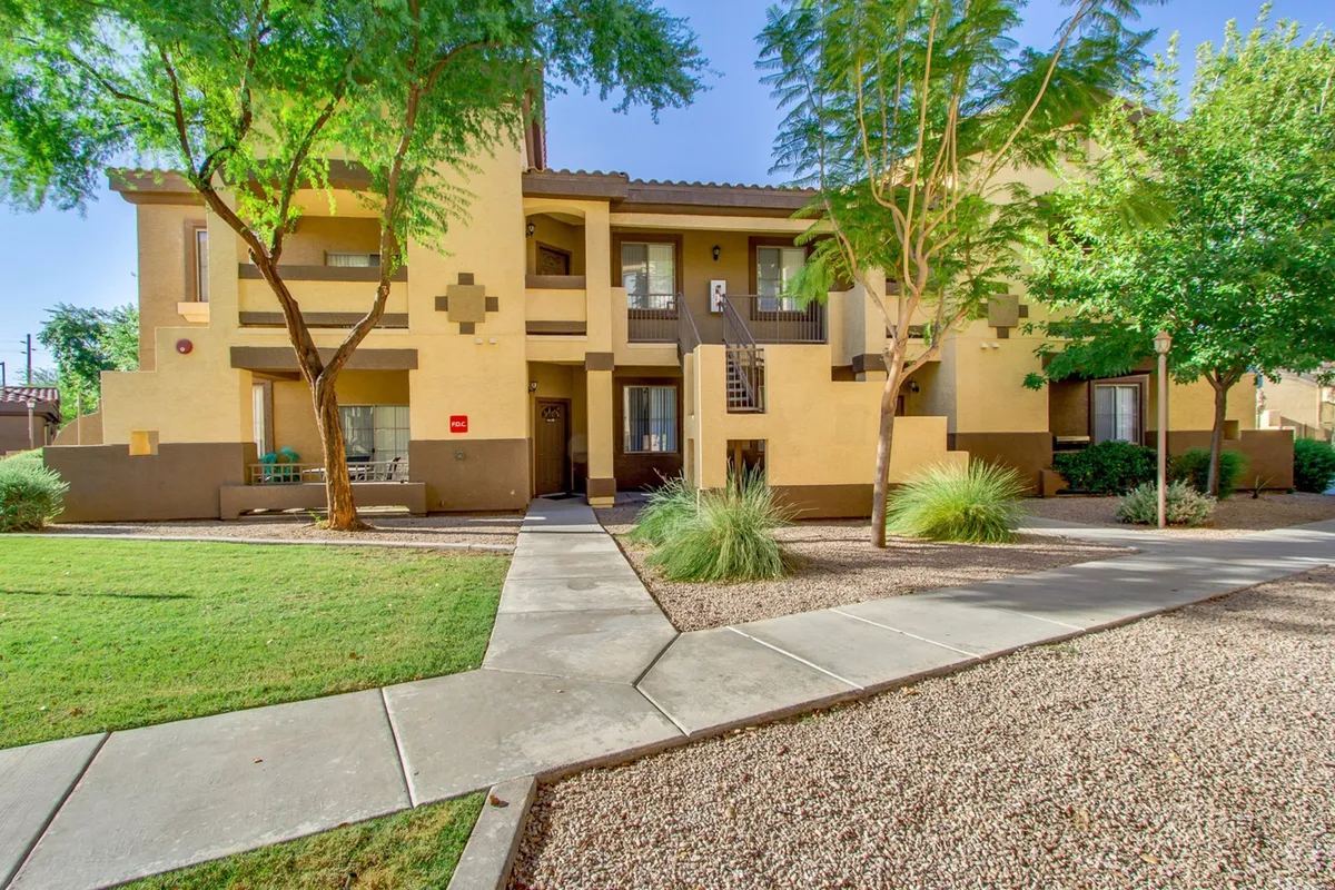 The gated entrance and landscaped grounds of the community, with walkways leading to the building. The scene conveys privacy, security, and a peaceful setting, with soft greenery and an inviting pathway.