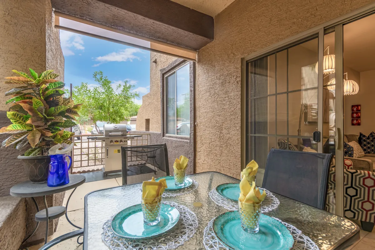 This image shows an outdoor patio area featuring a table set with drinks, a grill, and lush potted plants, suggesting a peaceful, private space for dining or relaxing. The setting is perfect for enjoying a morning coffee or a romantic sunset dinner in the fresh air, surrounded by greenery.