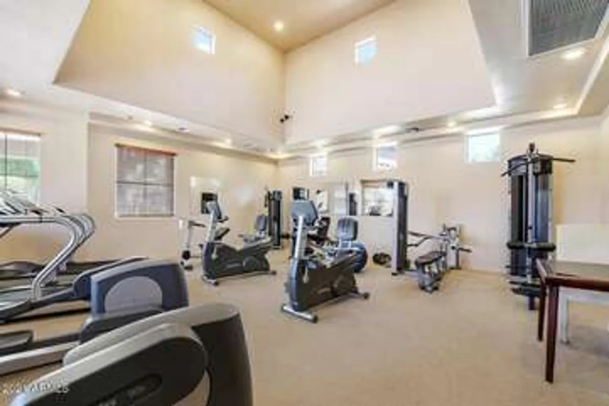 A fitness room featuring a variety of exercise machines, mirrors that add depth to the space, and windows that bring in light. The setup suggests opportunities for both individual workouts and community-oriented fitness classes.